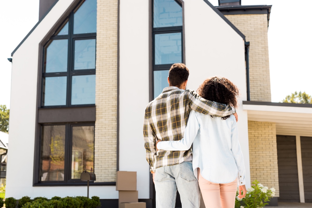 back view of african american couple hugging while looking at new house back view of couple hugging while looking at new house