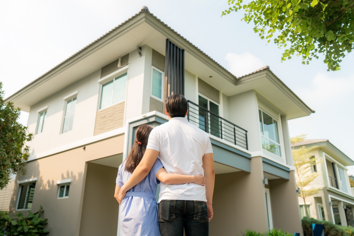 couple standing together looking at home with backs facing camera