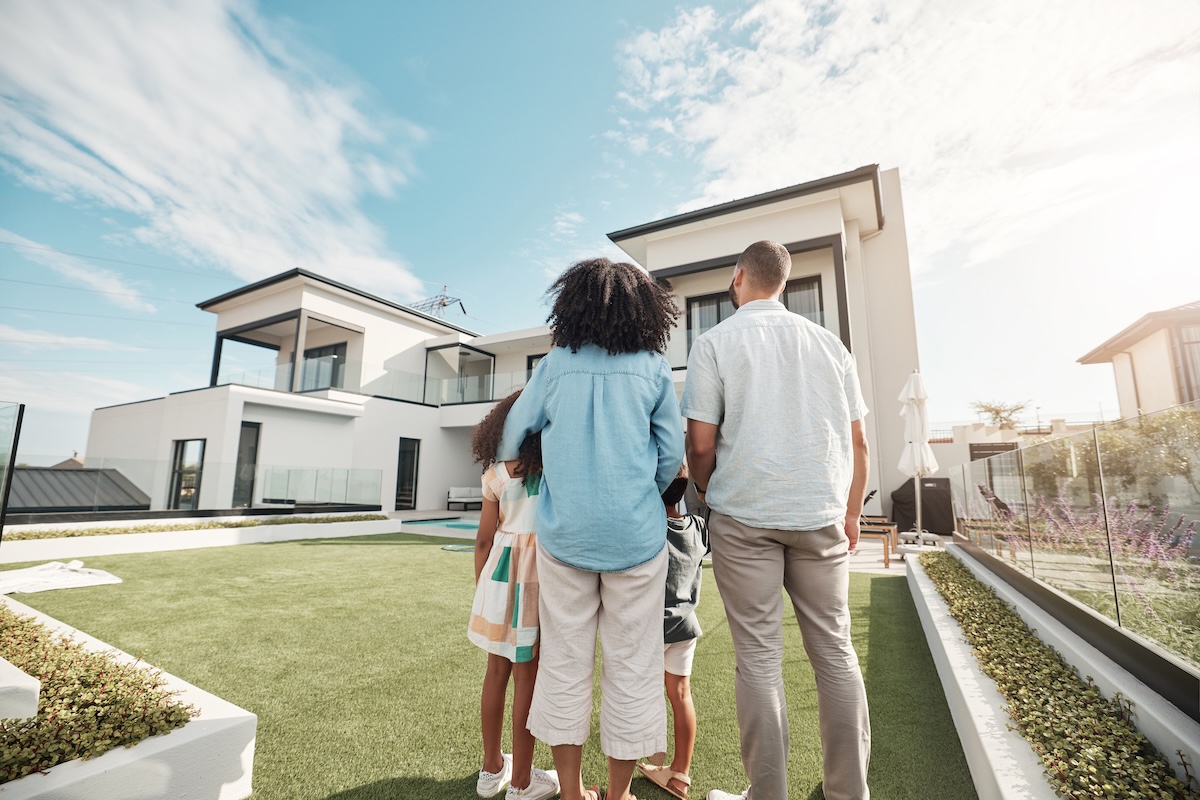 Love, new house and family in their backyard together looking at their property or luxury real estate. Embrace, mortgage and parents with their children on grass at their home or mansion in Canada. New house and family in their backyard together looking at their property