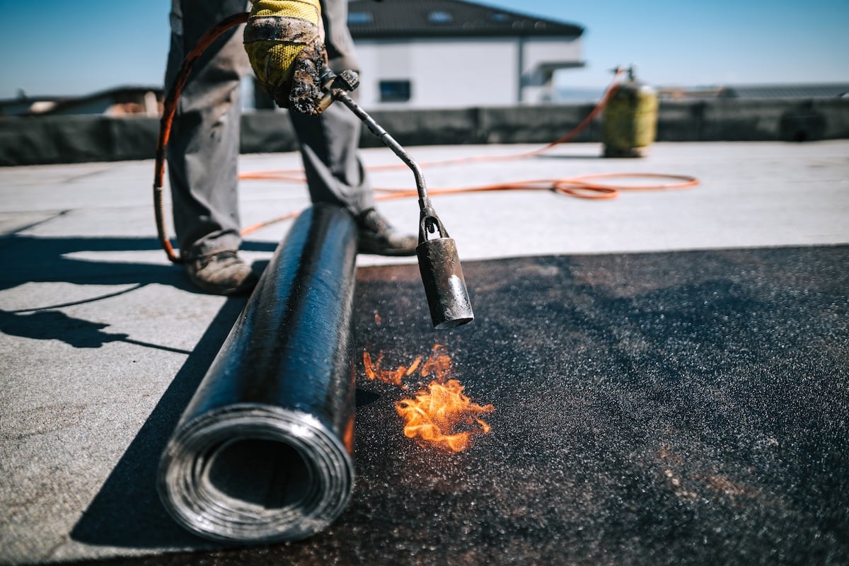 Professional workers insulating rooftop with bitumen membrane.