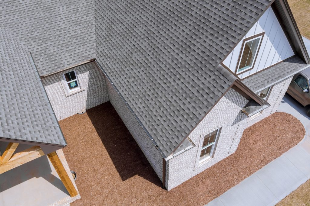 Roof of newly built house is being covered with asphalt shingles during construction while house is still being built