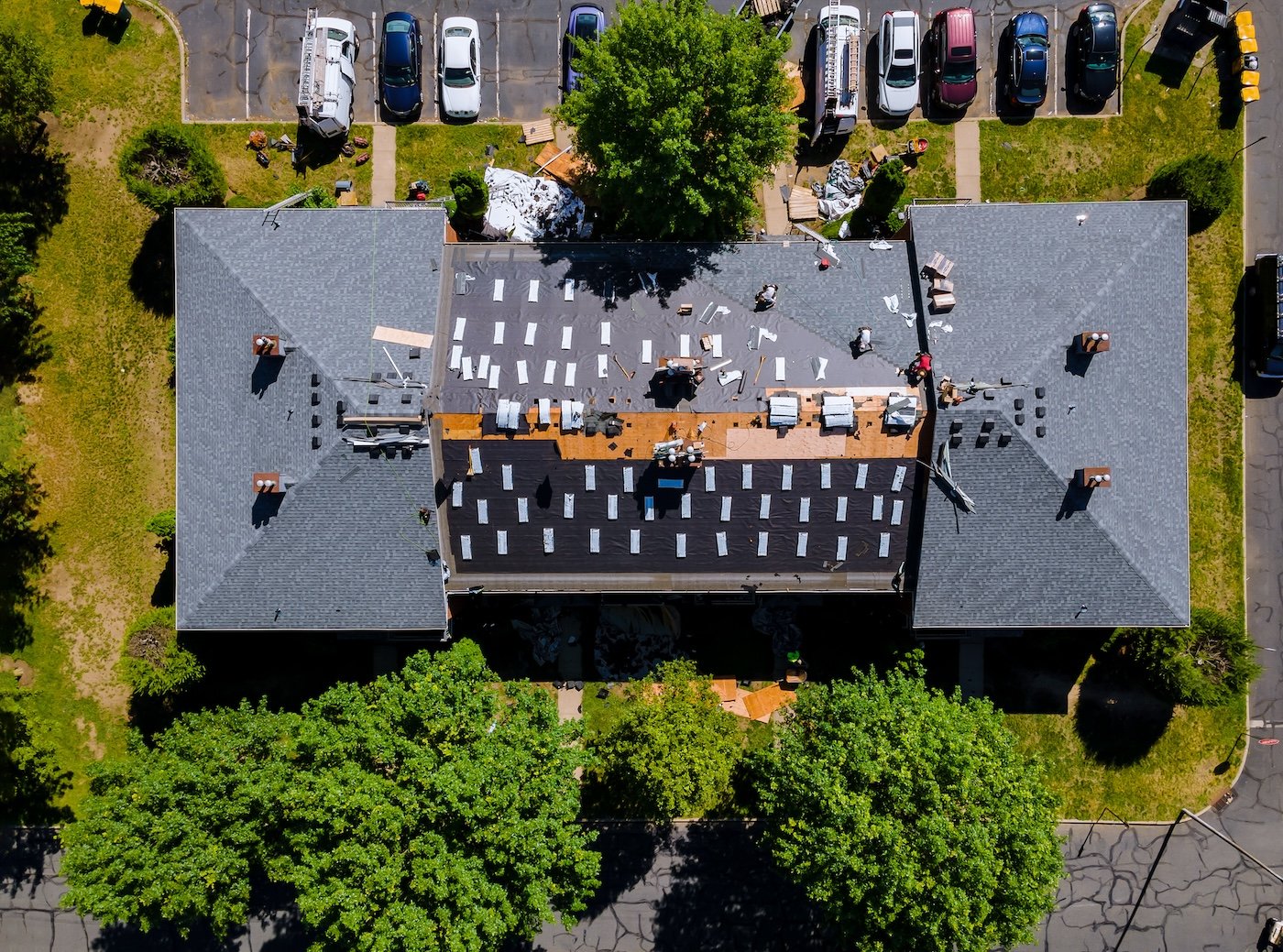 A roofer nailing shingles with air gun, replacing roof cover protection being applied, apartment development