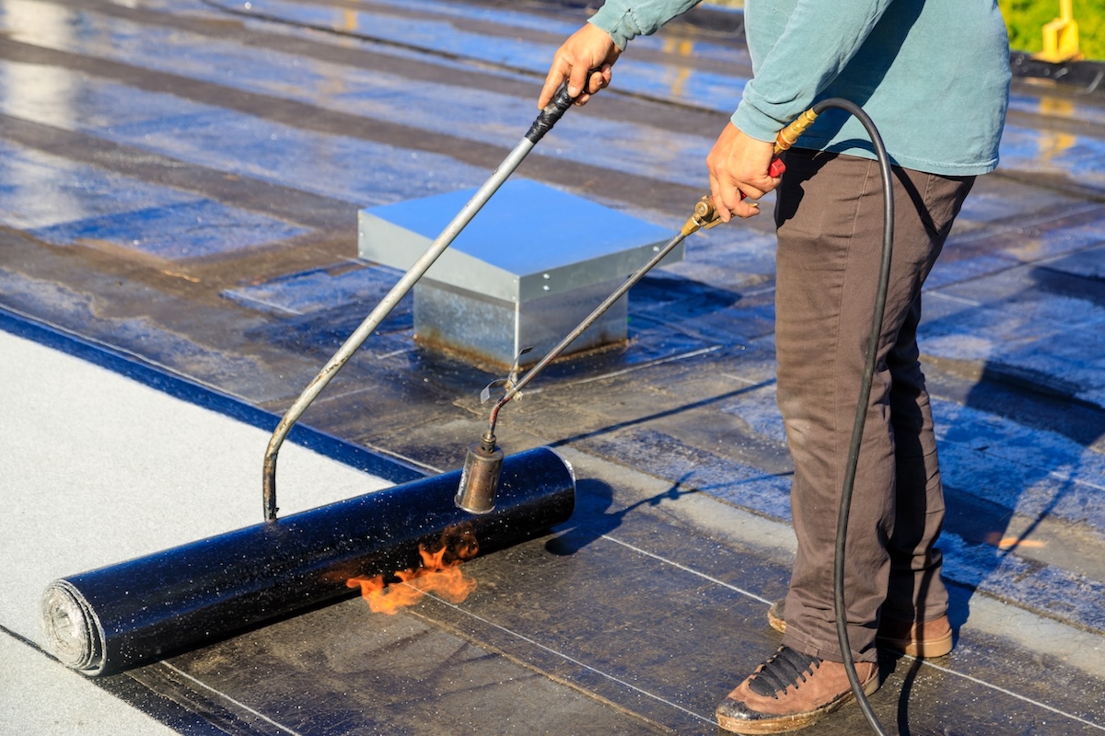 Roofer applying torch to membrane on flat roof