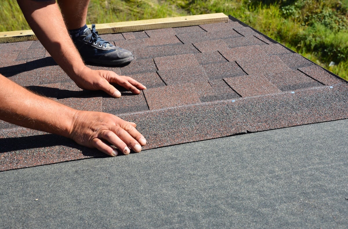 Roofing contractor lay asphalt shingles tiles on house rooftop.