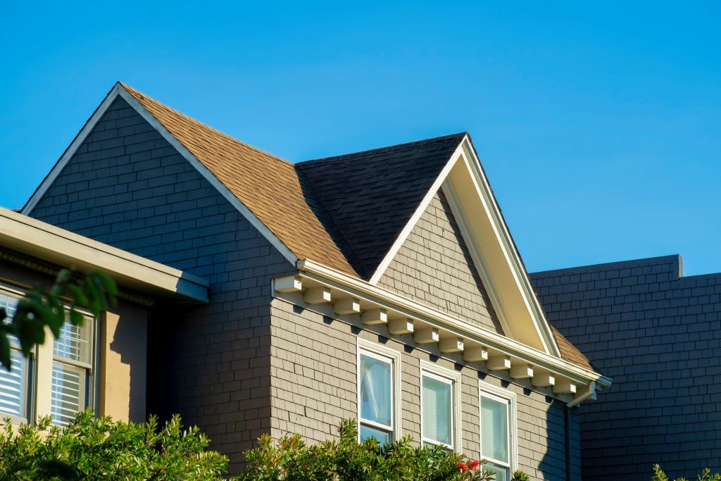 Double gable house with brown stucco with white window accent paint and visible blue windows and clear blue sky. In late afternoon sun in downtown neighborhood in san francisco california.
