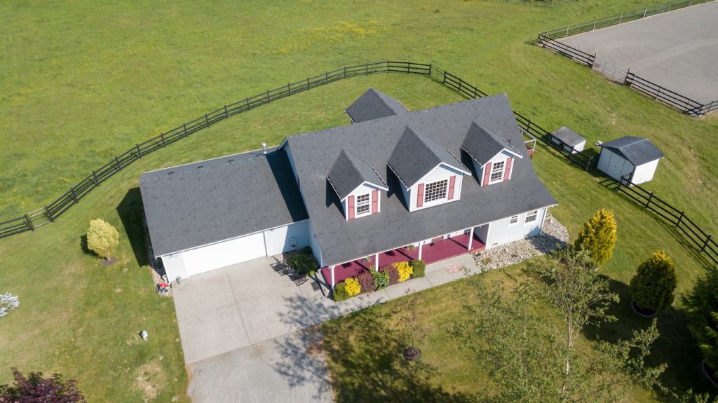 Drone photo of single family house with grey roof and large green grass yard.