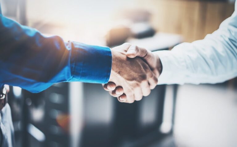 two men shaking hands with sunlight peeking through in the background / commercial roofing lakeside