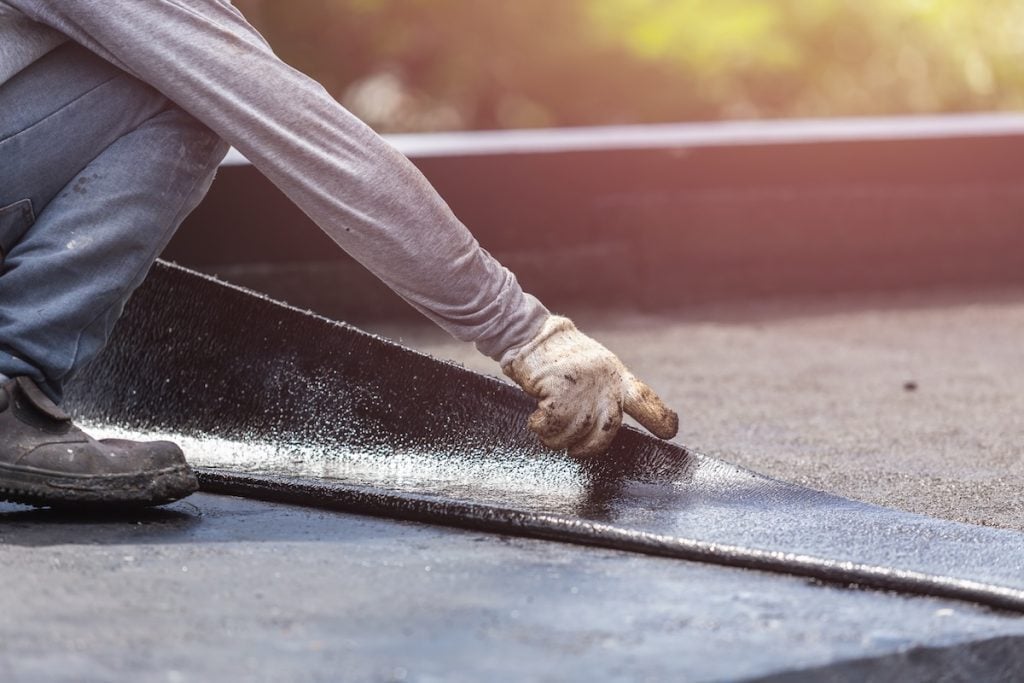 worker installing tar foil on the rooftop of building. Waterproof system by gas and fire torching