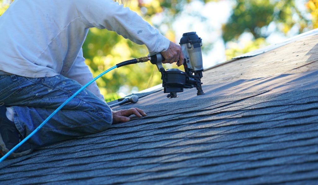 Roofer installing new shingles on roof using nail gun