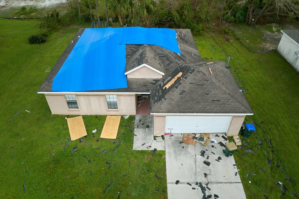 Top view of leaking house roof covered with protective tarp sheets against rain water leaks until replacement of asphalt shingles. Damage of building rooftop as aftermath of storm