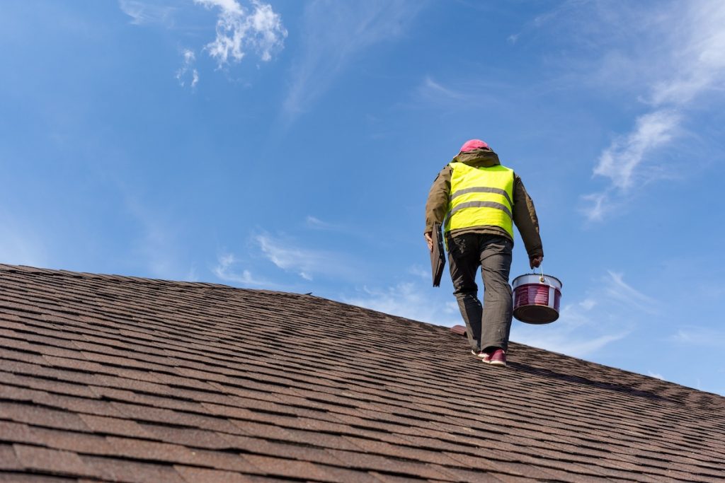 Unrecognizable and skilled workman in uniform standing on tile roof of new home under construction with equipment and instrument