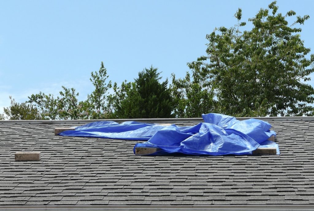 A blue plastic tarp over a roof leak provides temporary protection from further damage to a residence.