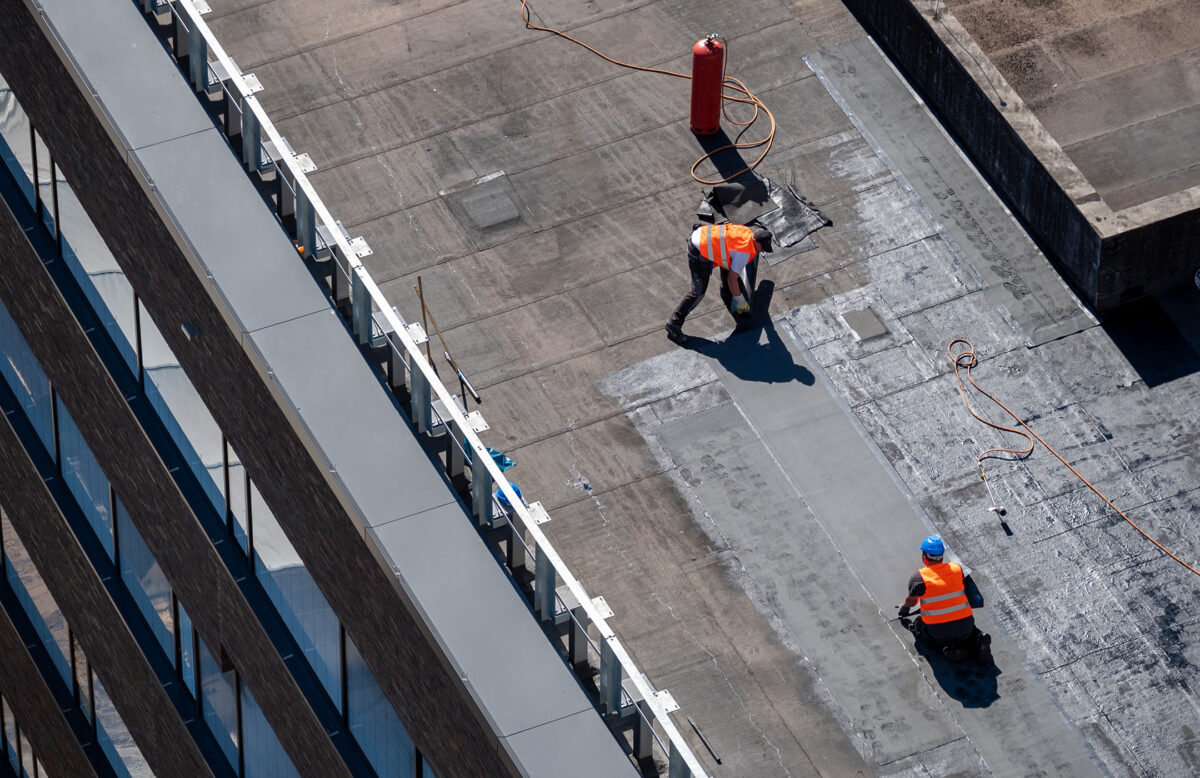 roof storm damage Birds eye view of a roof construction site. Professional bitumen waterproofing on a flat building.