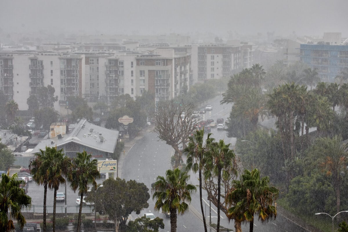super el nino effects Heavy rain falls along Via Marina in Marina del Rey, California, dramatically reducing visibility across the coastal community. Traffic moves through the downpour past palm trees and residential buildings, with the Foghorn Harbor Inn and The Cheesecake Factory restaurant visible along the roadway as intense rainfall obscures the distance.